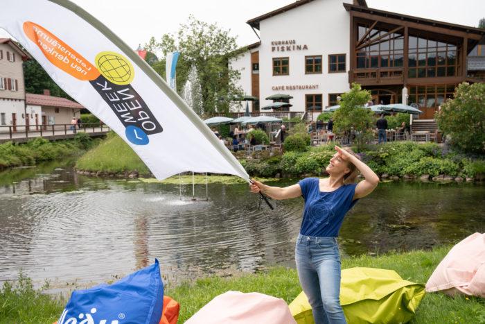 Catharina Fischer von Realizing Progress hält eine OpenWeek-Fahne in der Hand vor dem Kurhaus in Fischen